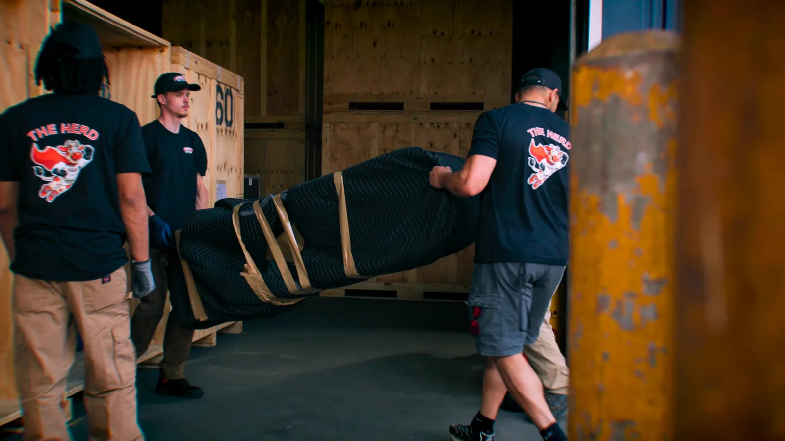 Two movers carry a wrapped item past storage vaults inside the warehouse.